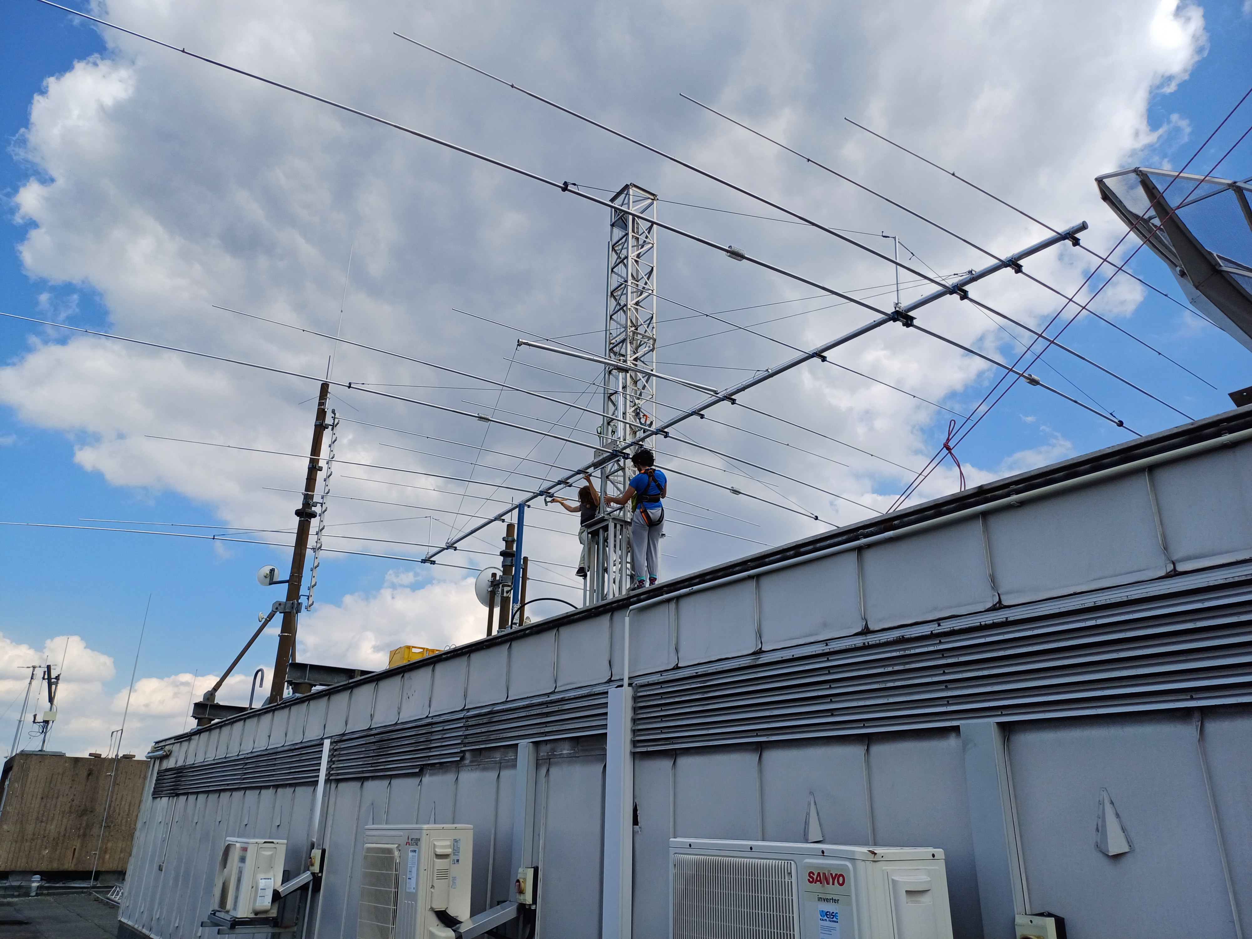 Über das gesamte Bild: Antenne. Darunter arbeiten DL7OAR und DK3NN, in Kletterzeug gesichert, am Einspeisepunkt der Antenne